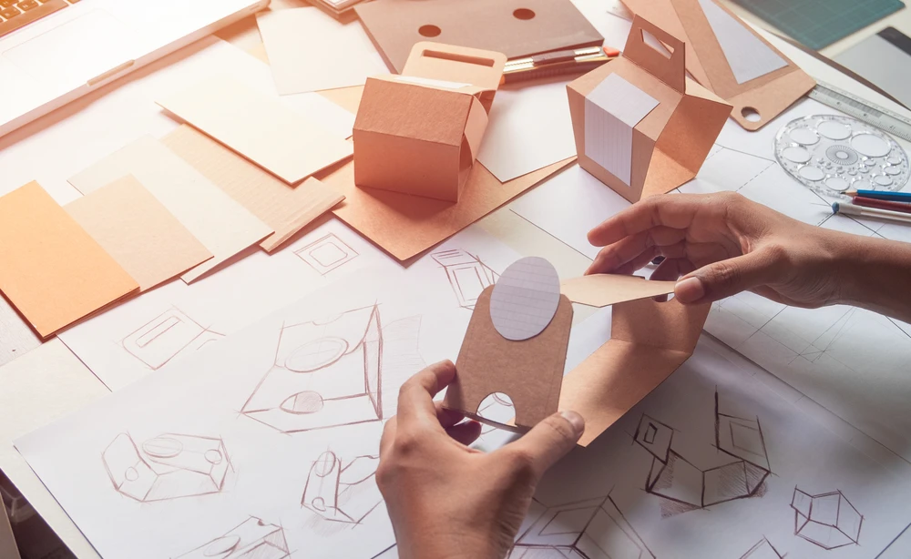 Espace de travail intérieur avec mains manipulant prototype en carton brun