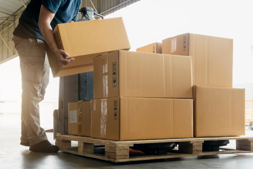 Entrepôt industriel avec employé en tenue de travail manipulant des colis en carton ondulé