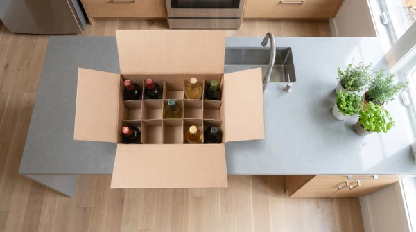 Cinq bouteilles de vin align&eacute;es sur surface claire avec emballages cylindriques en carton kraft brun, bouchons en li&egrave;ge dispos&eacute;s devant chaque bouteille
