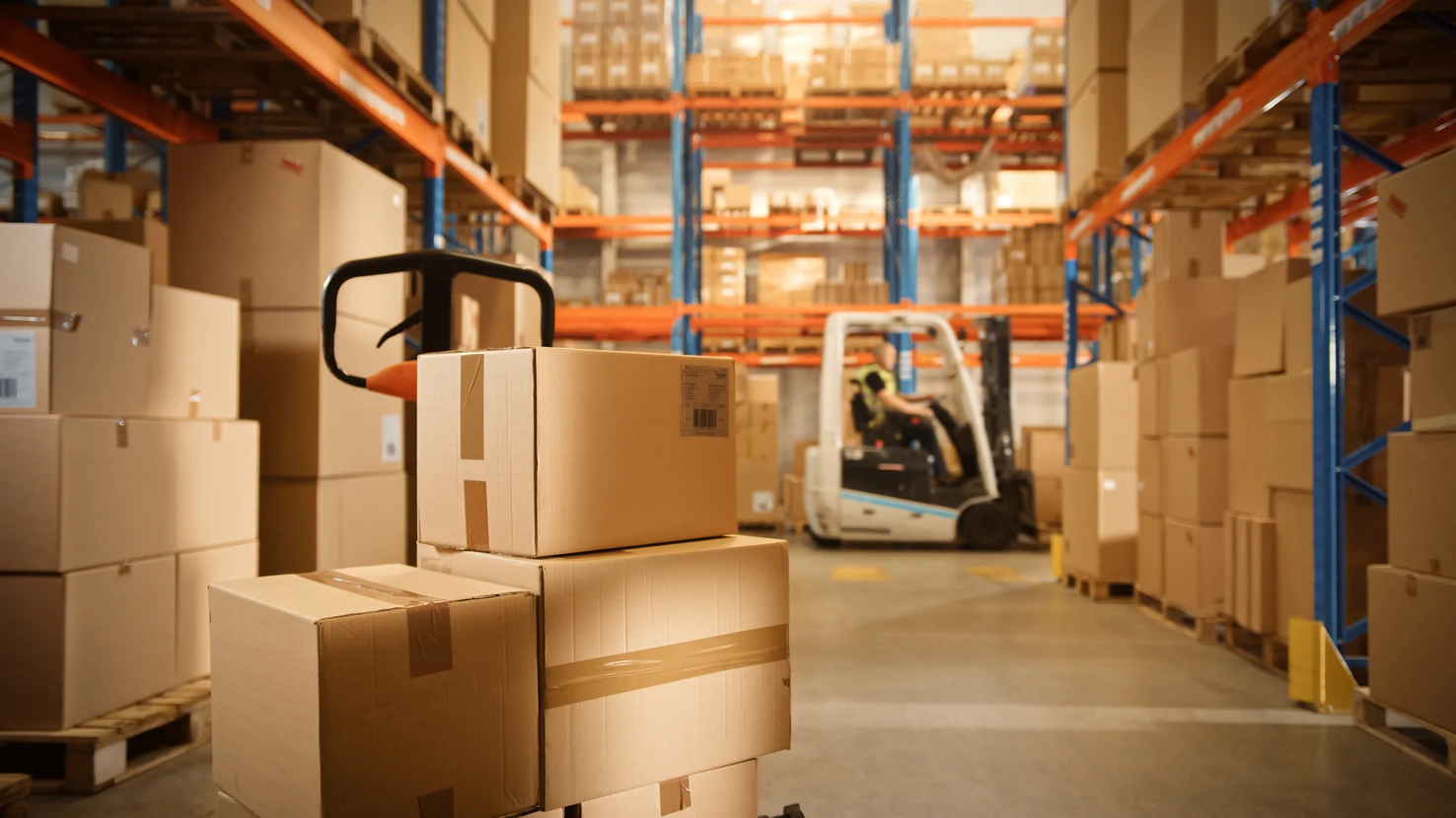 Entrepôt industriel avec employé en tenue de travail manipulant des colis en carton ondulé
