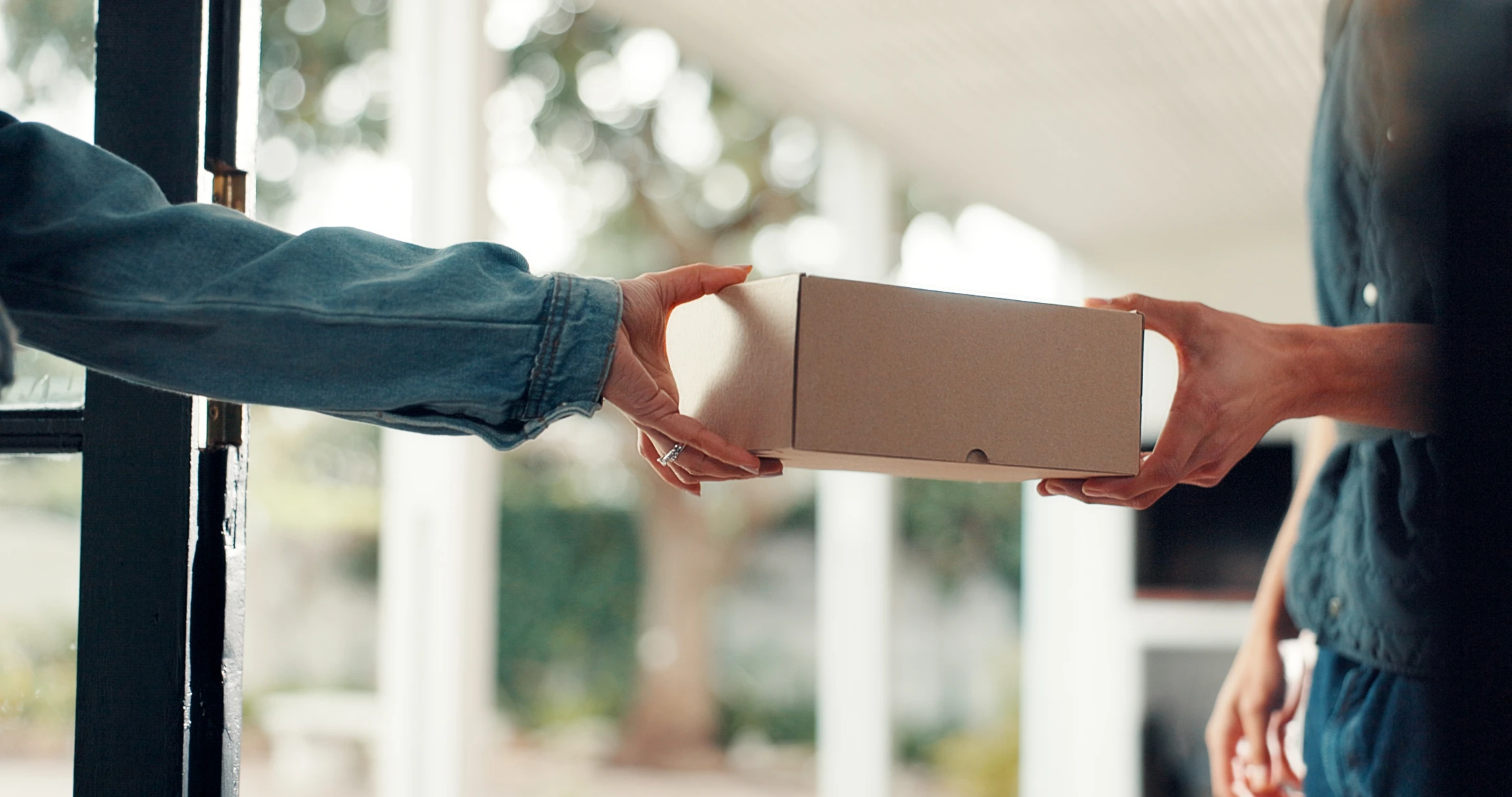 Livreur en uniforme professionnel tenant un colis carton et un terminal de paiement électronique portable dans un environnement intérieur neutre